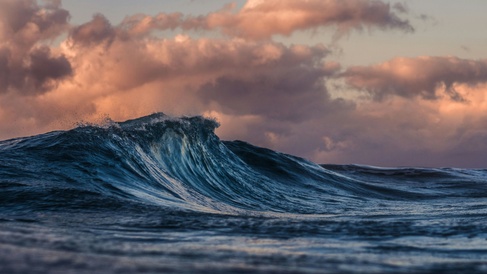 Dramatic waves on the sea with pink-orange clouds on the horizon